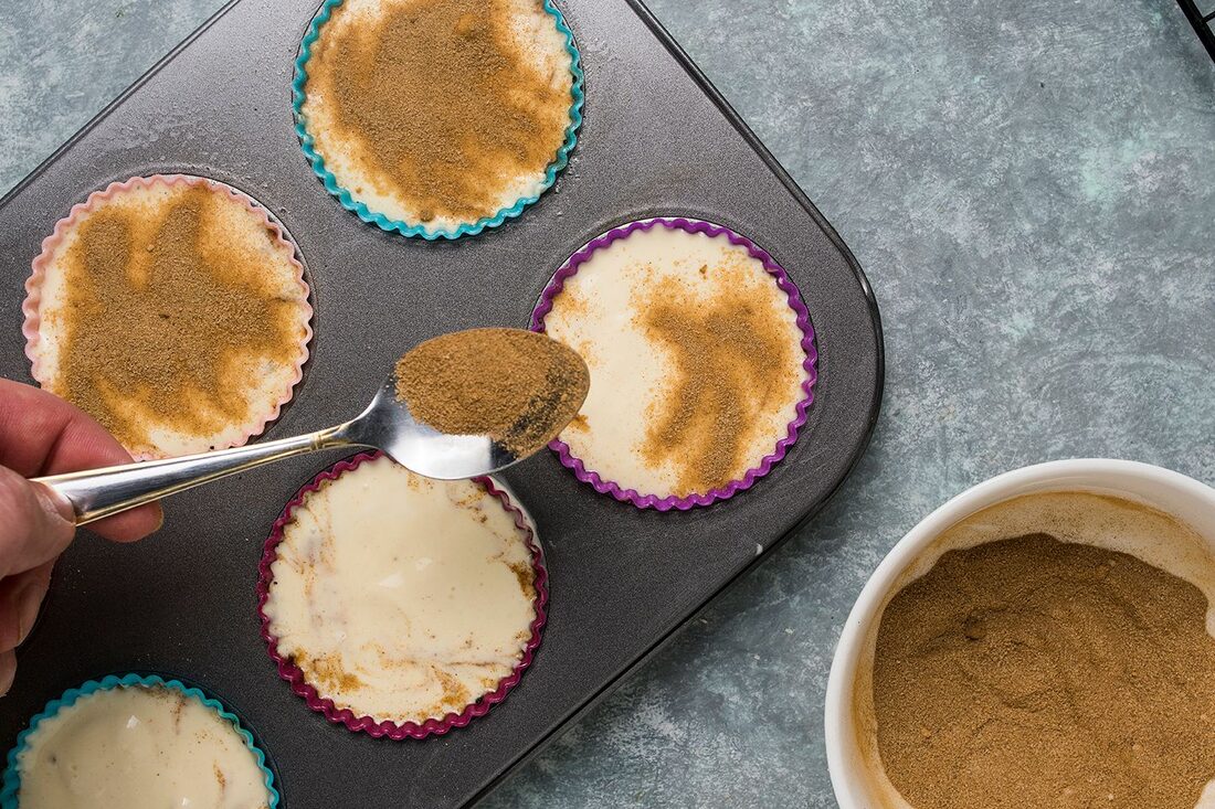 Hands adding cinnamon to a tray of mini cheesecakes during a process shot